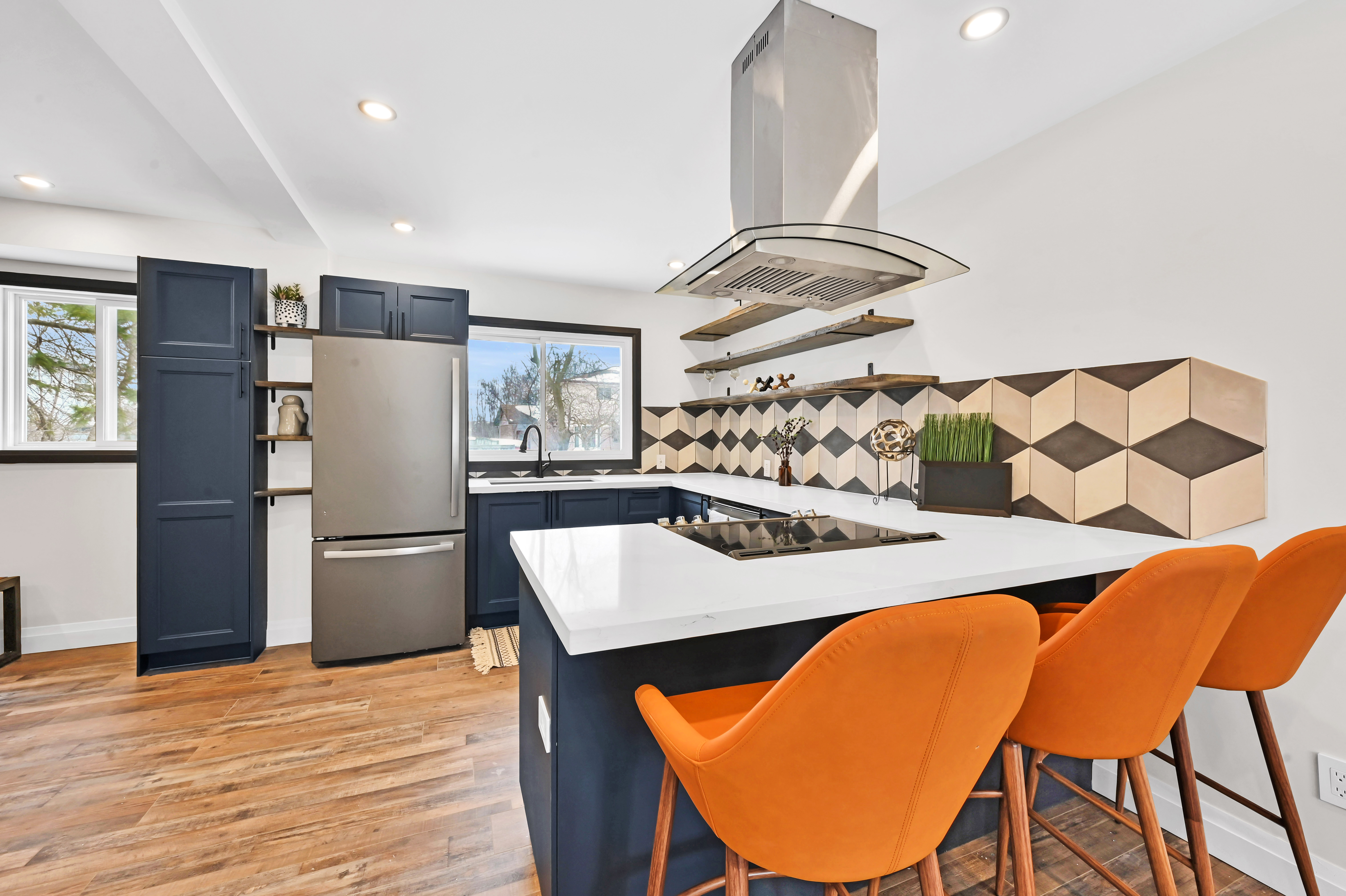 Stunning finished kitchen with dramatic geometric backsplash, bold orange chairs, and excellent natural lighting — Kron, Hamilton | MTC Renovations